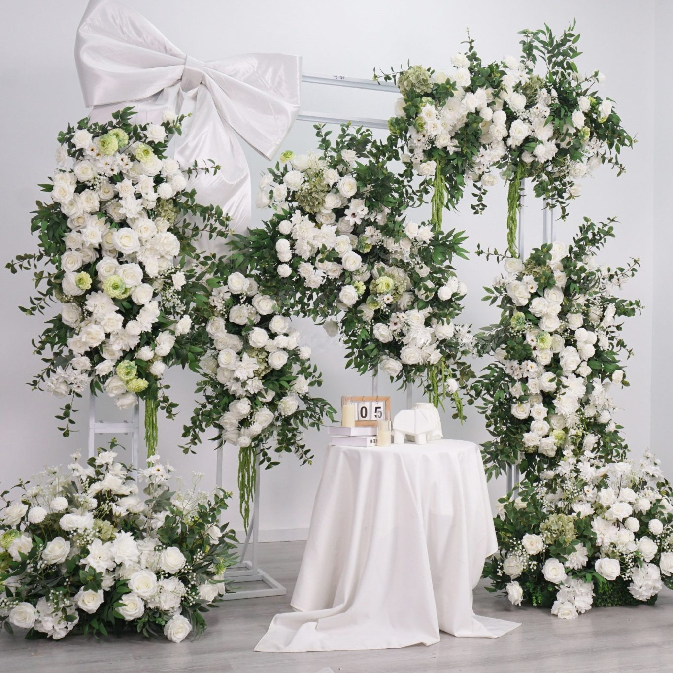 Grace - Broken Arch and Floral Frame A floral wedding backdrop with white flowers and greenery, adorned with a large bow.