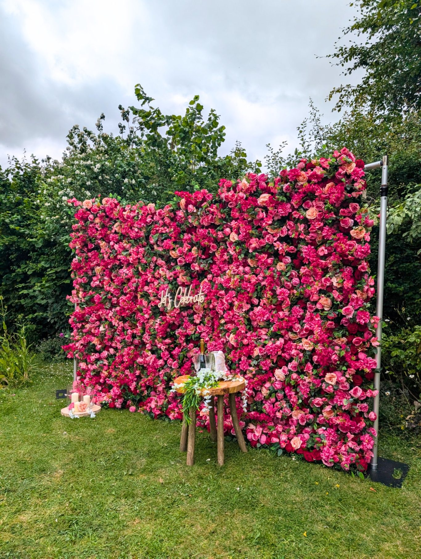 Edith - Size: Large A vibrant pink floral backdrop with a small table decorated in front, set in a garden.