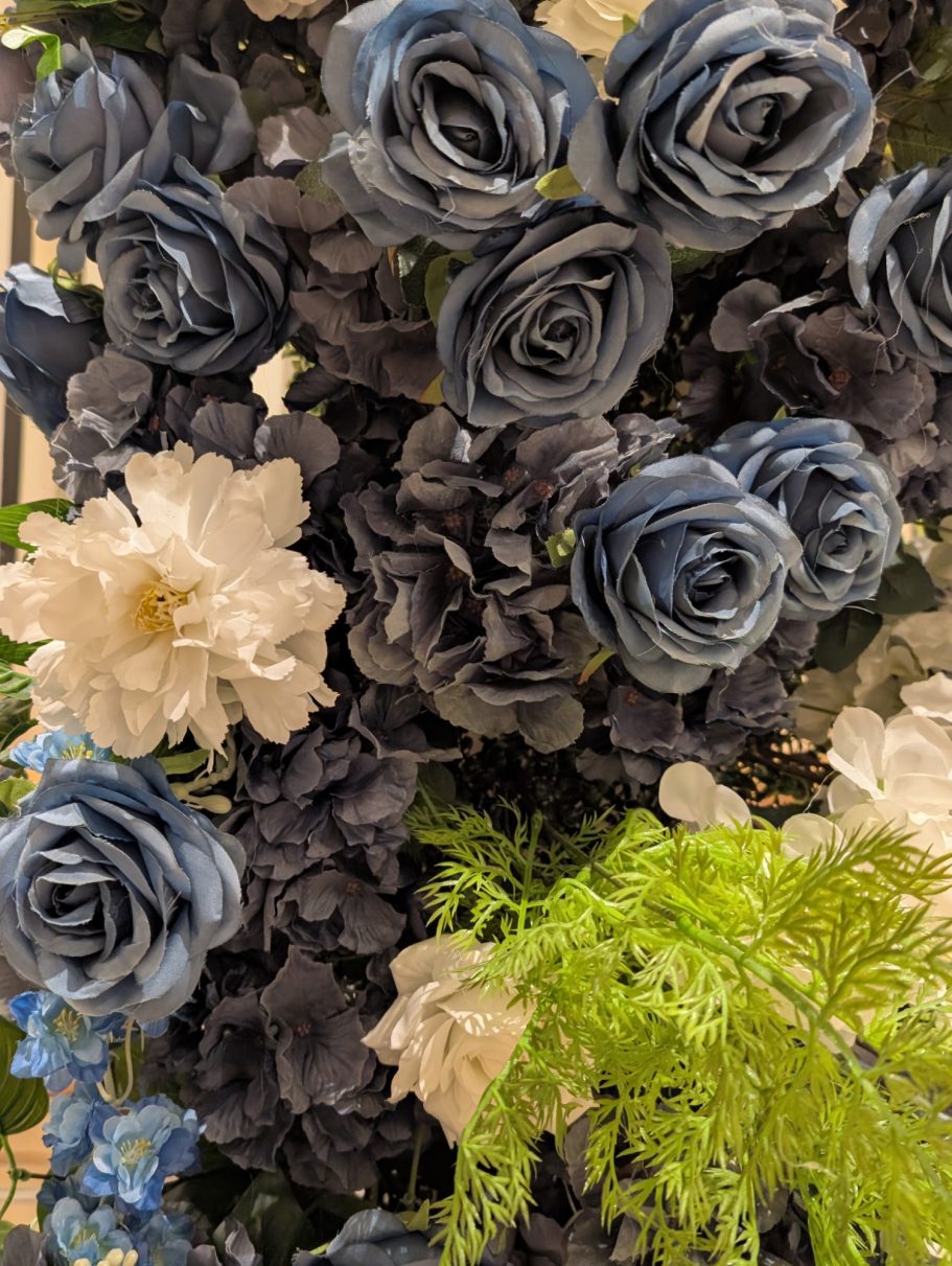 Isabella Arch - Detail A close-up of blue and white artificial flowers with green foliage.