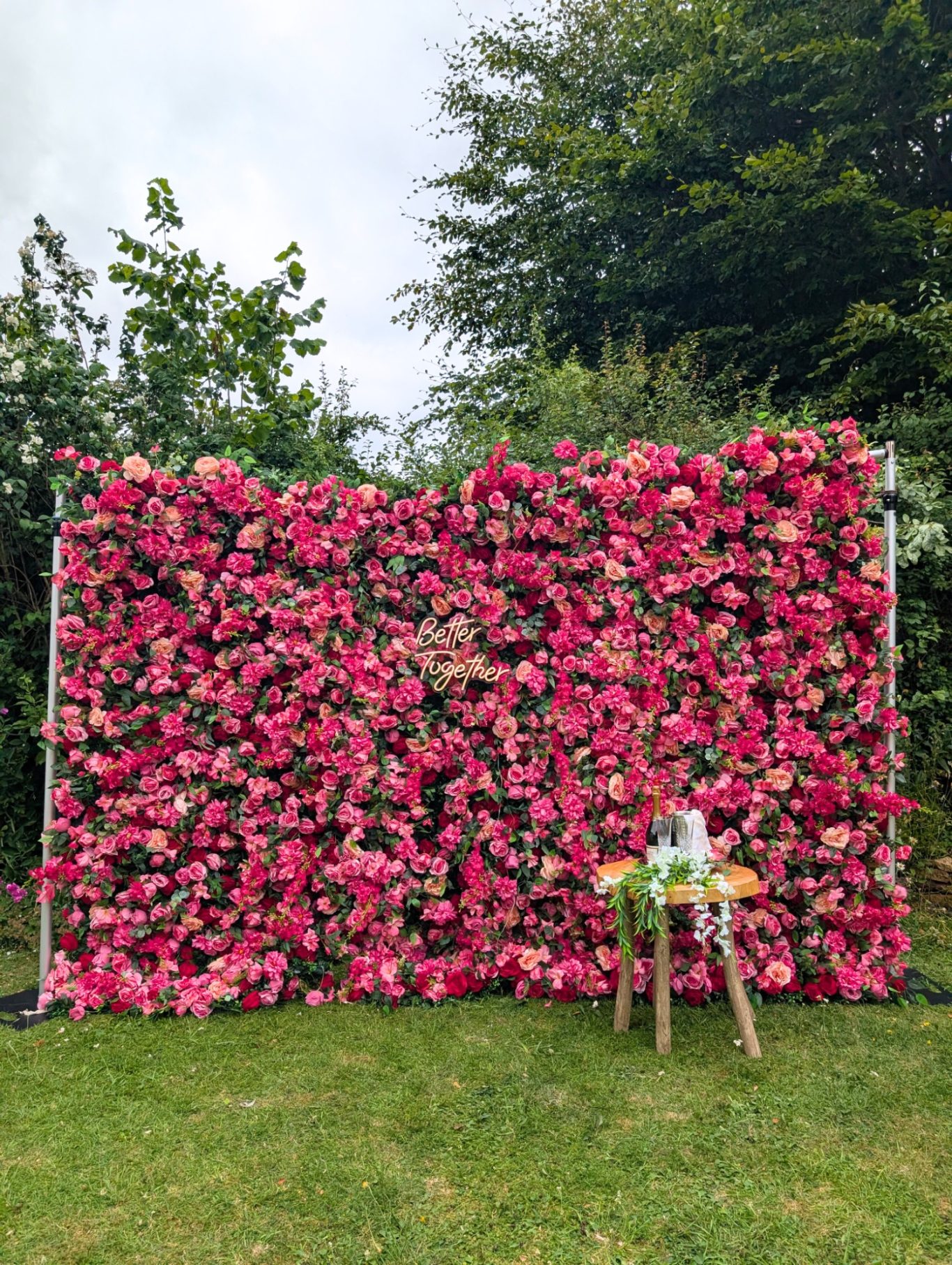 Edith - Size: Large A vibrant floral backdrop of pink flowers with a small table and vase in front.