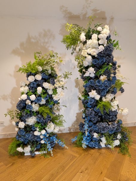 Two floral arrangements featuring blue and white flowers, displayed on wooden flooring.