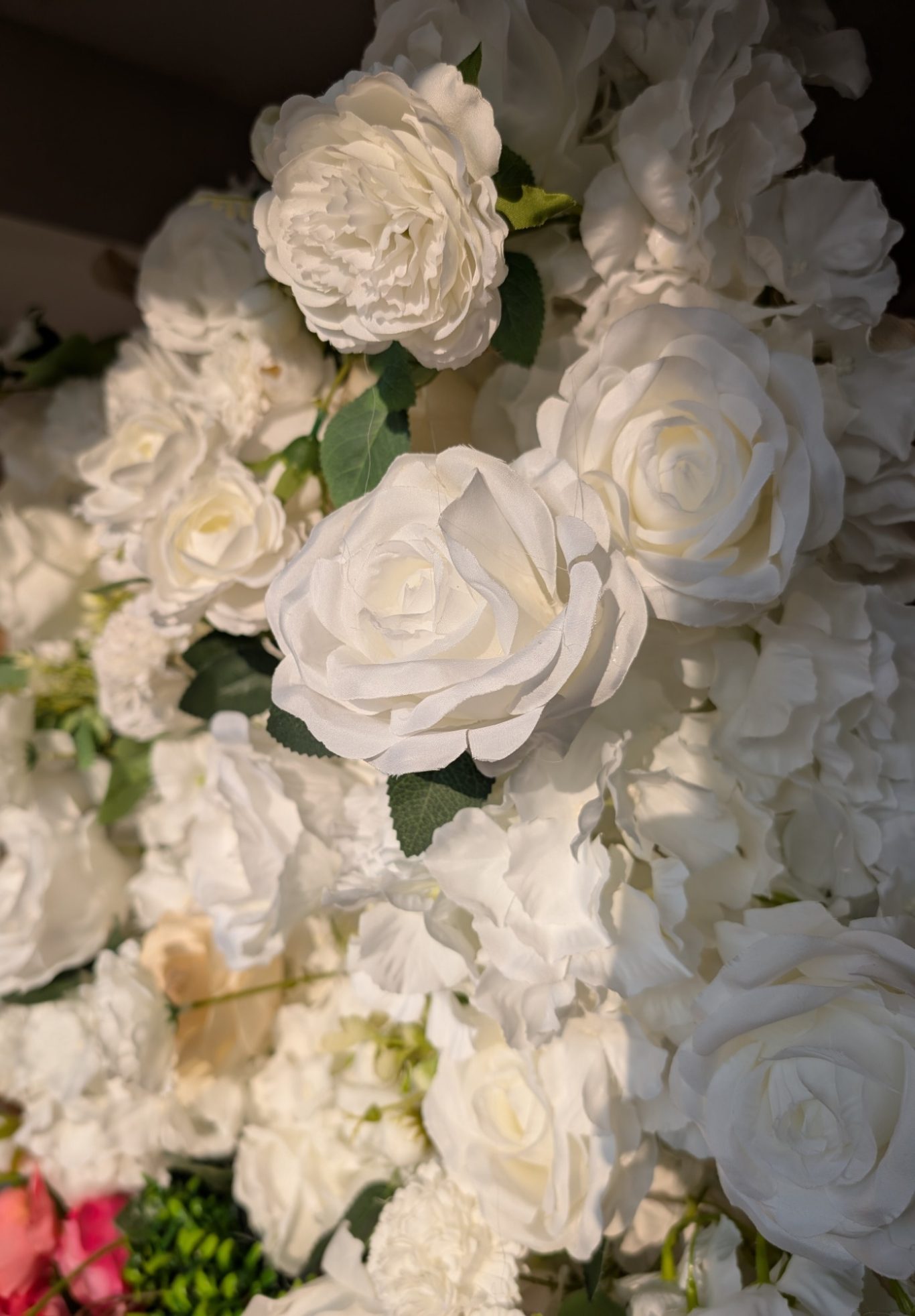 Joy - Detail during the golden hour A close-up of large, white artificial roses with green leaves.